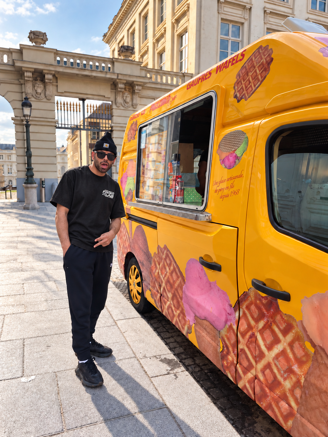 ALexander T. Rose  in a black  OpenForm FTL (FromTheLab) t-shirt stands next to a Brussels Pascalino ice cream truck decorated with waffle and ice cream illustrations, parked on a cobblestone street in front of a historic building.
